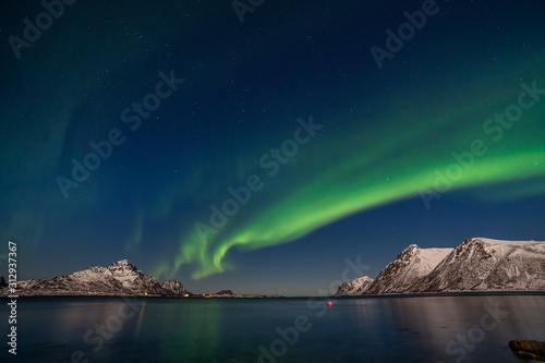 beautiful aurora borealis. Green northern lights. Starry sky with polar lights. winter landscape with aurora, sea with sky reflection and snowy mountains. © Tatiana