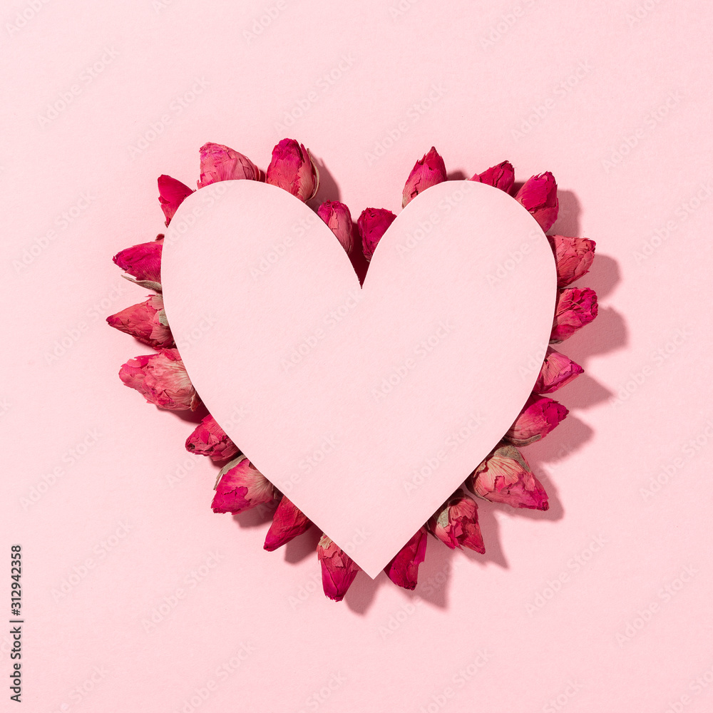 Conceptual background of Valentine's day, pink heart made of paper on white background, dry rose flowers arranged on the contour of the heart shape.