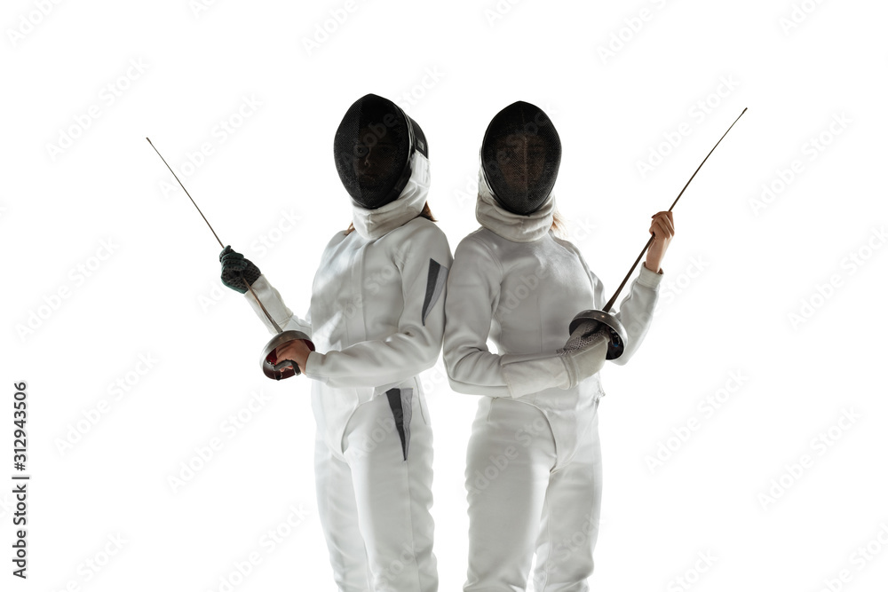 Teen girls in fencing costumes with swords in hands isolated on white studio background. Young female models practicing and training in motion, action. Copyspace. Sport, youth, healthy lifestyle. Teen girls in fencing costumes with swords in hands isolated on white studio background. Young female models practicing and training in motion, action. Copyspace. Sport, youth, healthy lifestyle.
