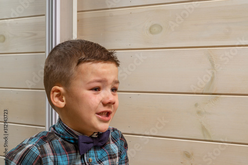 Foto A 4 years old boy in a blue clerical shirt is crying on a light wooden background