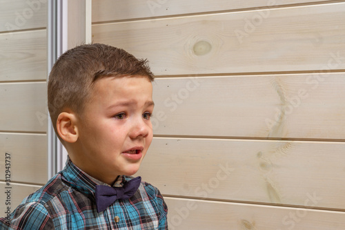 Bild auf Leinwand A 4 years old boy in a blue clerical shirt is crying on a light wooden background