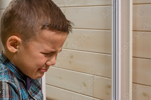 Foto A 4 years old boy in a blue clerical shirt is crying on a light wooden background