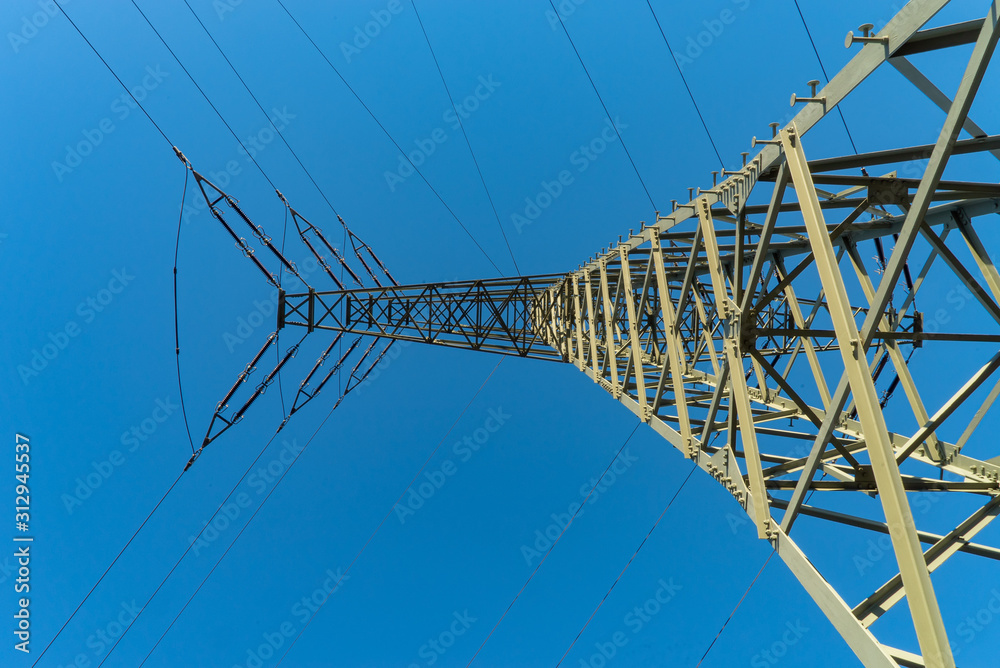 Seitenarm mit Leitungen am Strommast von unten im Sonnenlicht mit blauem Himmel