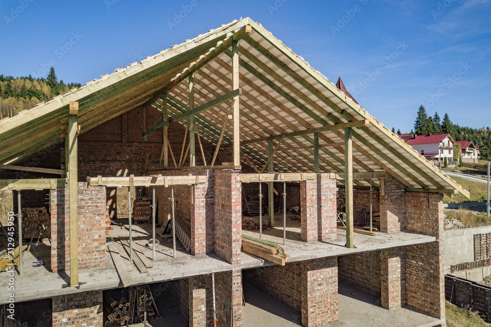 Wooden frame of new roof on a brick big house under construction. Wooden frame of new roof on a brick big house under construction.