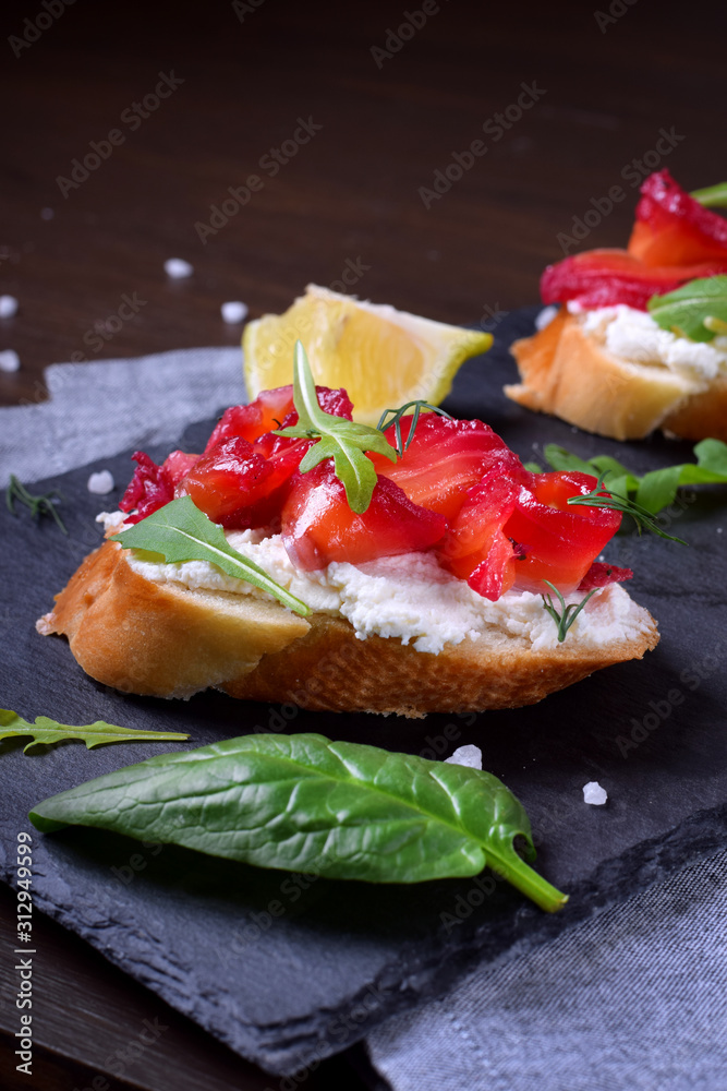 Trout Gravlax on the slices of white bread with ricotta topped with greenery on the stone platter. Nordic cuisine meal Trout Gravlax on the slices of white bread with ricotta topped with greenery on the stone platter. Nordic cuisine meal