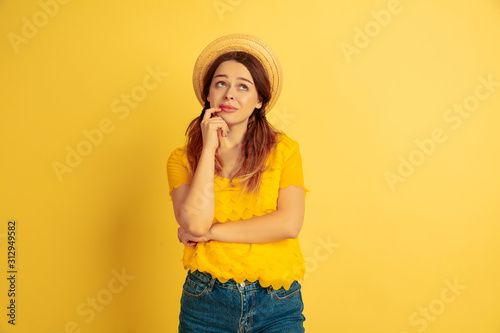 Dreamful, thoughtful. Caucasian woman's portrait on yellow studio background. Beautiful female model in hat. Concept of human emotions, facial expression, sales, ad. Summertime, travel, resort.