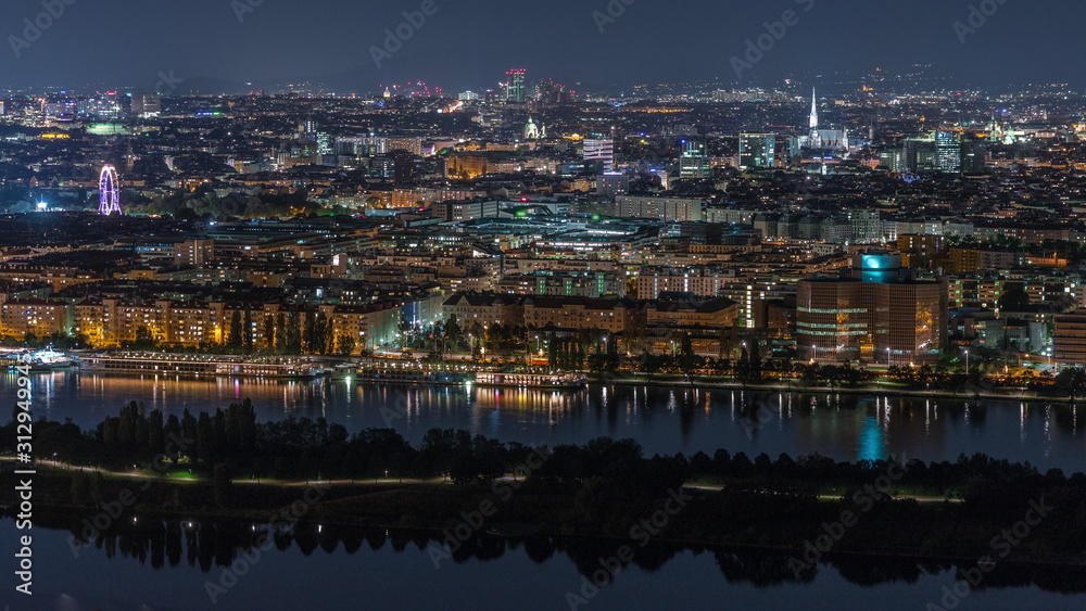 Aerial panoramic view over Vienna city with skyscrapers, historic buildings and a riverside promenade night timelapse in Austria.
