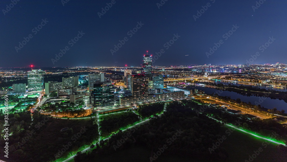 Fototapeta premium Aerial panoramic view over Vienna city with skyscrapers, historic buildings and a riverside promenade night timelapse in Austria.