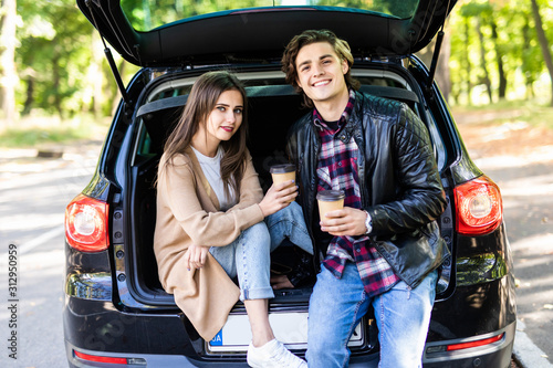 Beautiful young couple sitting with coffee in car trunk © F8  \ Suport Ukraine