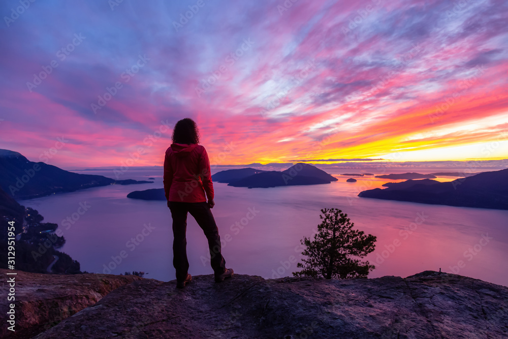 Adventurous Caucasian Girl standing on top of a mountain during a colorful winter sunset. Taken on Tunnel Bluffs Hike, North of Vancouver, BC, Canada.