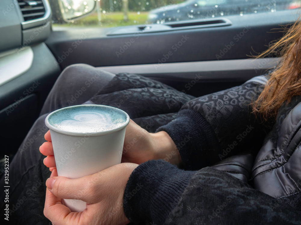 Blue matcha latte art in eco friendly paper cup. Main color 2020 year concept. A cup of coffee female hands in car. Minimal composition.