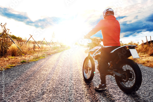 Junger Motorradfahrer auf einer Straße schaut in den Sonnenuntergang