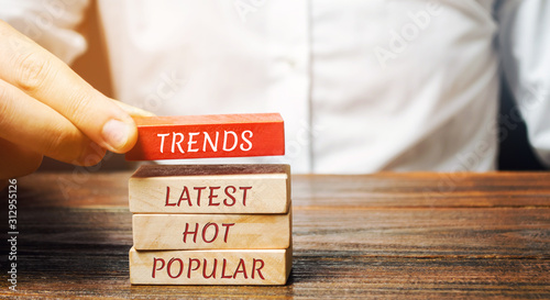 Businessman puts wooden blocks with the words Trends, latest, hot, popular. Popular and relevant topics. New ideological trends. Recent and latest trend. Evaluation methods.