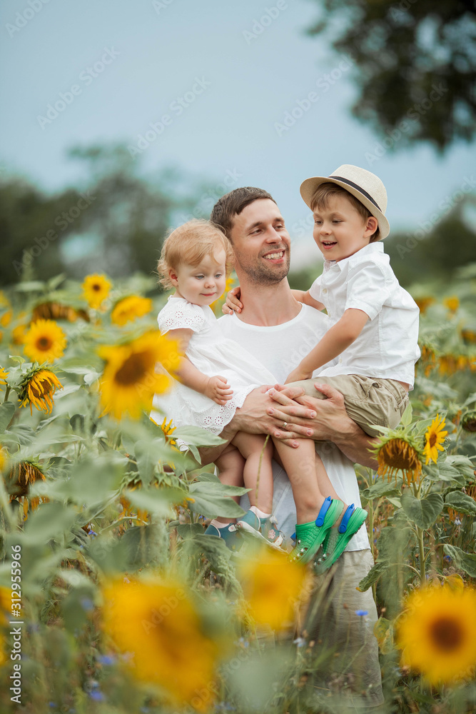 A happy family walks in a field of sunflowers. Young handsome dad with two children in a sunflower field. A happy family walks in a field of sunflowers. Young handsome dad with two children in a sunflower field.