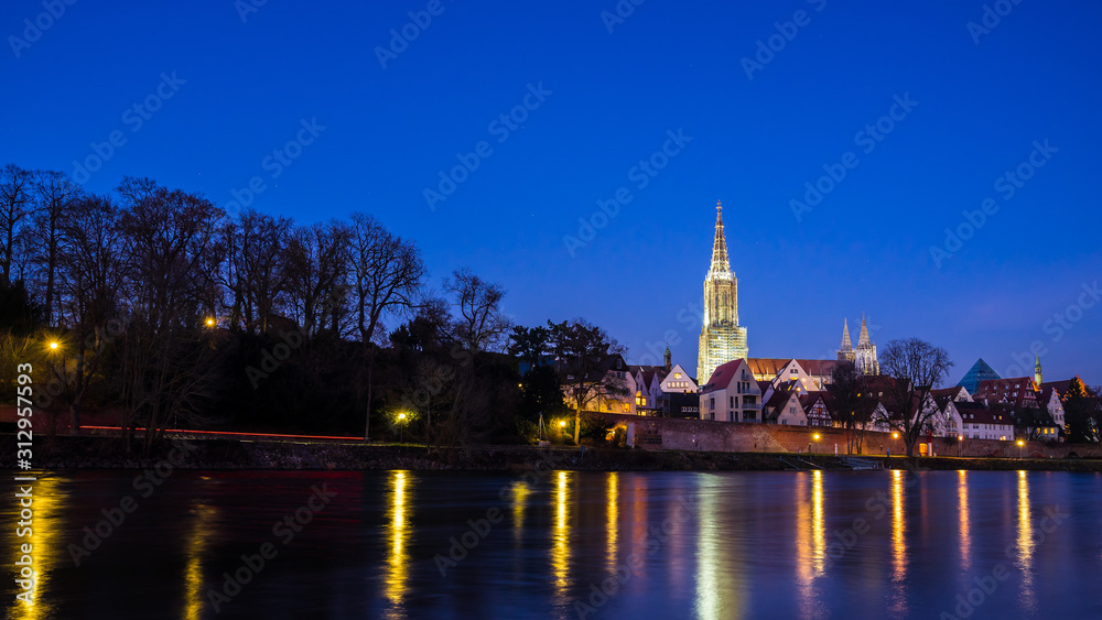 Germany, Ulm city skyline, cityscape and minster cathedral behind water of danube river by night with starry sky
