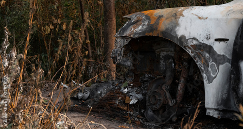 Fototapeta Naklejka Na Ścianę i Meble -  The car after the fire. Burned out engine. Burnt car without a hood, ash and garbage after a fire. Arson of a car near a forest near the city. Traffic accident and vandalism concept. 