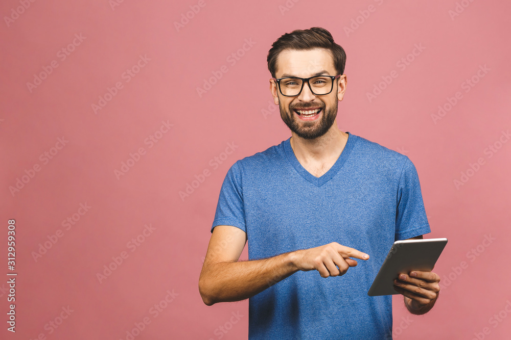 Happy young man in casual standing and using tablet over pink background Happy young man in casual standing and using tablet over pink background