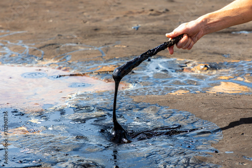A man's hand stirring liquid asphalt with a wooden stick at Pitch Lake, the largest natural deposit of bitumen in the world. La Brea, Trinidad island, Trinidad and Tobago