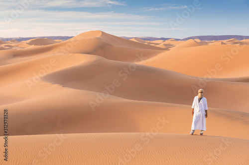 Bedouin on way through sandy desert. Beautiful sunset with big dunes on Sahara  Morocco. Silhouette nomad man. A touareg with his traditional clothes and turban. Picturesque background nature concept