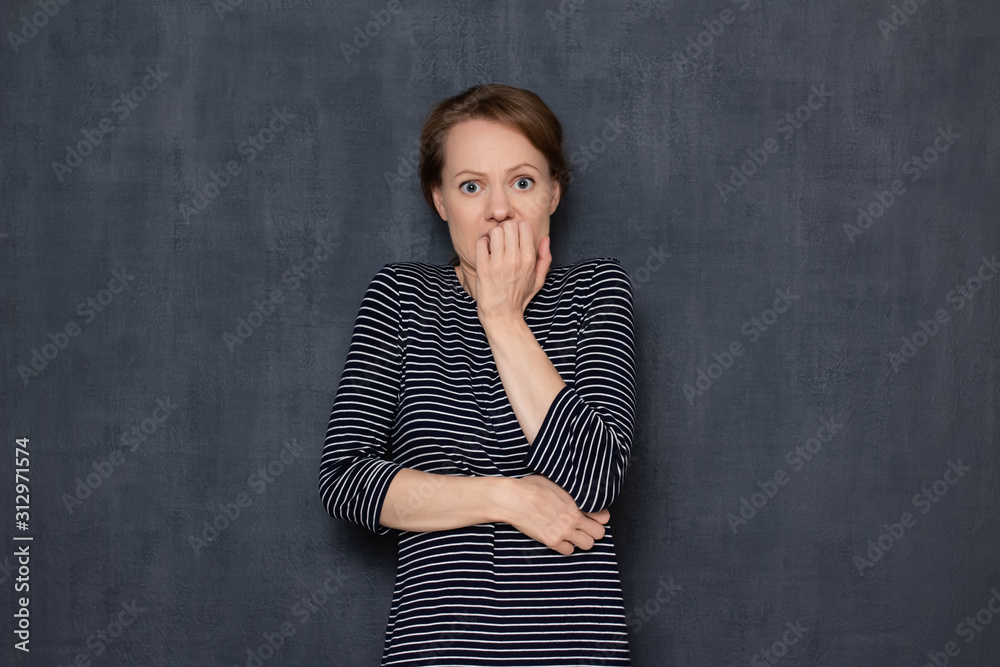Portrait of shocked frightened young woman biting nails in panic
