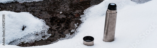 vacuum flask on snow near flowing mountain stream, panoramic shot © LIGHTFIELD STUDIOS