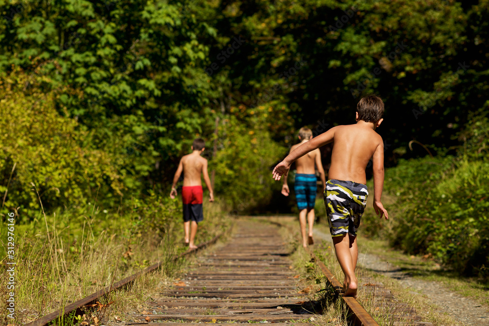 Boys in swim trunks walking along sunny railroad tracks in woods Boys in swim trunks walking along sunny railroad tracks in woods