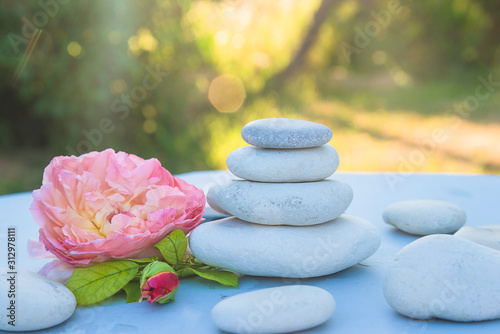Sea stones pyramid, rose flower head on the white table in the summer garden on sunlight
