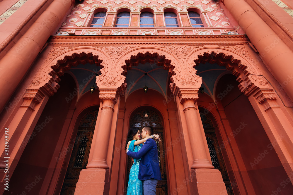 hug a couple in love near a red building with incredible archite