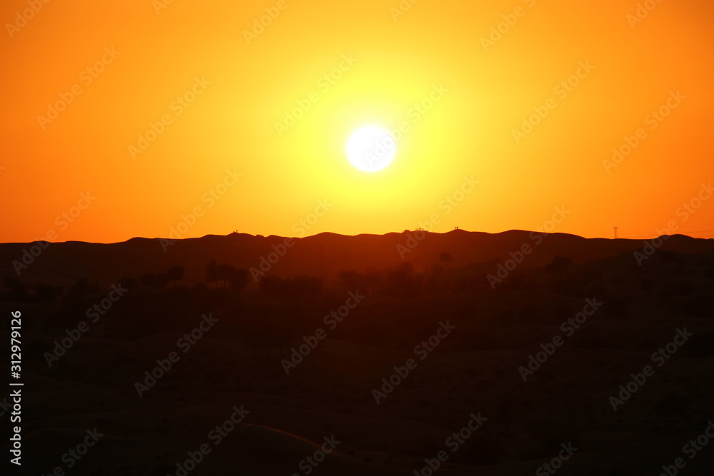 Orange sunset in the desert with silhouette of mountains