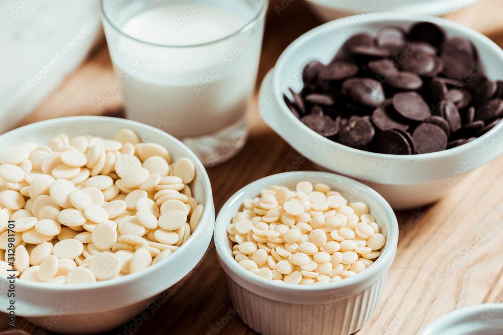 selective focus of white chocolate chips in bowls near glass with milk selective focus of white chocolate chips in bowls near glass with milk