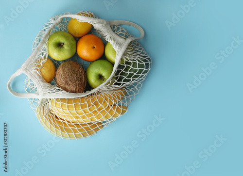 Net bag with fruits on light blue background, top view. Space for text