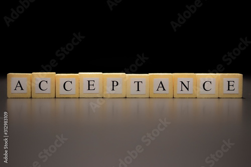 The word ACCEPTANCE written on wooden cubes isolated on a black background...