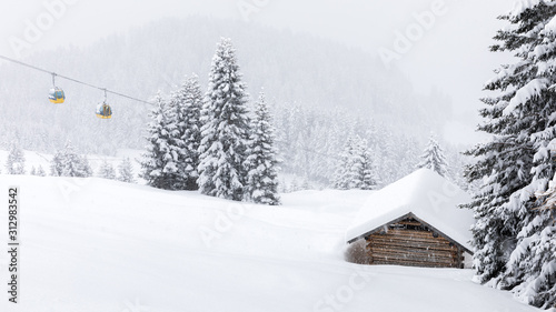 Winter scene in mountains with snow falling and snowy tree and yellow ropeway cabins