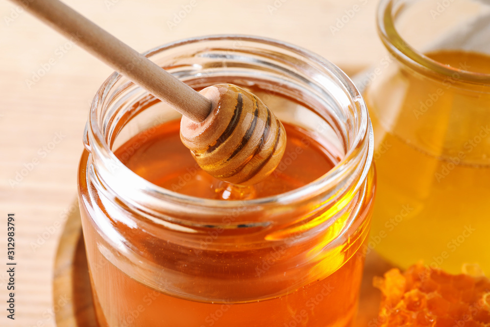Dripping tasty honey from dipper into glass on table, closeup Dripping tasty honey from dipper into glass on table, closeup