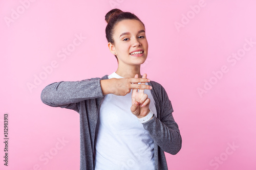 Hashtag, internet popularity. Portrait of cheerful trendy teenage girl with bun hairstyle in casual clothes showing hash symbol with fingers, smiling at camera. studio shot isolated on pink background