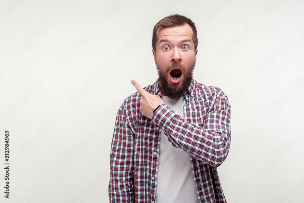 Wow, look there! Portrait of shocked bearded man in casual plaid shirt pointing finger to the side up, empty space for advertisement, looking surprised amazed. studio shot isolated on white background Wow, look there! Portrait of shocked bearded man in casual plaid shirt pointing finger to the side up, empty space for advertisement, looking surprised amazed. studio shot isolated on white background