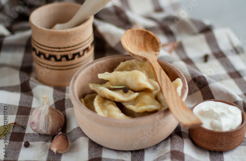 Wooden plate of varenikes with spice, sour cream and wooden spoon on the checkered tablecloth