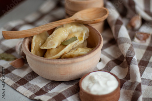 Wooden plate of varenikes with spice, sour cream and wooden spoon on the checkered tablecloth