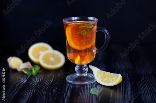 Glass transparent cup of tea with lemon, ginger and mint on the black background