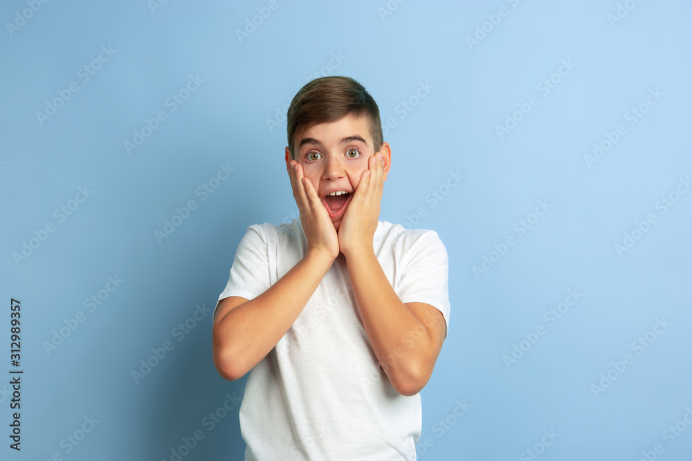 Crazy happy, astonished. Caucasian boy portrait isolated on blue studio background. Beautiful teen male model in white shirt posing. Concept of human emotions, facial expression, sales, ad. Crazy happy, astonished. Caucasian boy portrait isolated on blue studio background. Beautiful teen male model in white shirt posing. Concept of human emotions, facial expression, sales, ad.