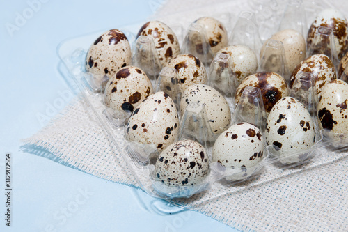 quail eggs in a plastic transparent tray for eggs on a light blue background, linen fabric, copy space. Easter background, close-up photo
