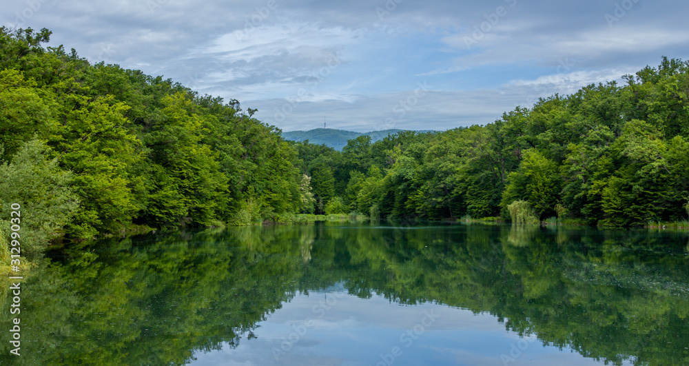 Panorama of a lake in Maksimir park with green tree reflections and a mountain Medvednica in Zagreb