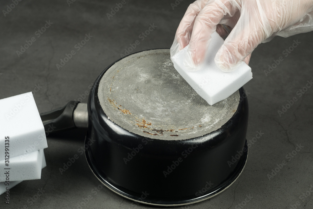 Person scrubbing an old pot with melamine magic sponge, eco friendly cleaning
