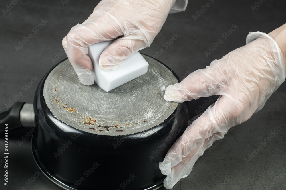 Hands in gloves cleaning old pot with eco friendly magic sponge, no detergent house cleaning