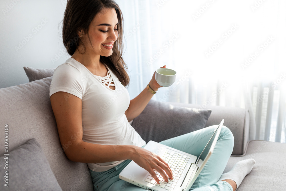Surfing the net at home. Side view of attractive young African woman working on laptop and smiling while sitting on the couch at home. Happy pretty woman using laptop sitting on cosy sofa Surfing the net at home. Side view of attractive young African woman working on laptop and smiling while sitting on the couch at home. Happy pretty woman using laptop sitting on cosy sofa