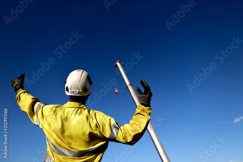 Rigger wearing a glove standing raising using a hand signal by moving finger slowly to direct communication with crane driver to move the boom up at construction site, Sydney, Australia    photo