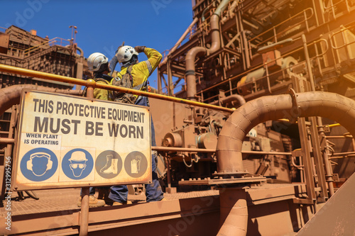 Personnel protective equipment (PPE) must be worn sign with defocused of construction workers wearing white hard hat at the background while working on the running plant construction site Perth