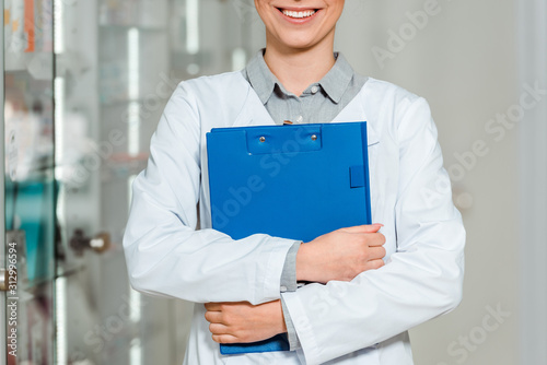 Cropped view of smiling pharmacist holding clipboard in drugstore