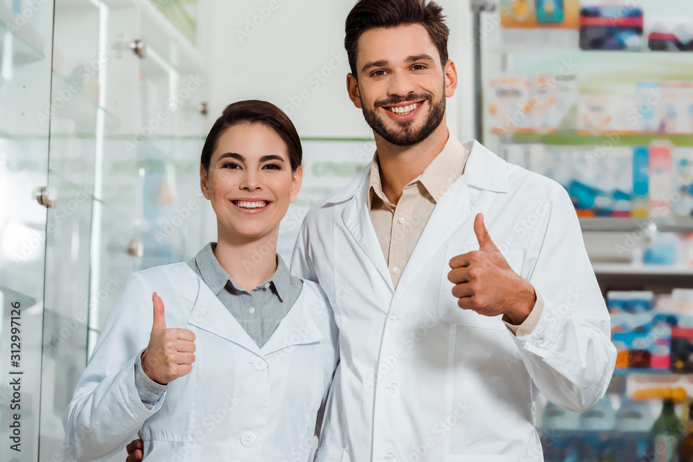 Pharmacists smiling at camera and showing thumbs up in pharmacy Pharmacists smiling at camera and showing thumbs up in pharmacy