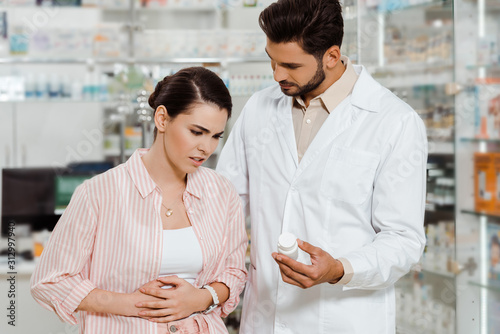 Pharmacist showing pills to customer with stomach disease in drugstore